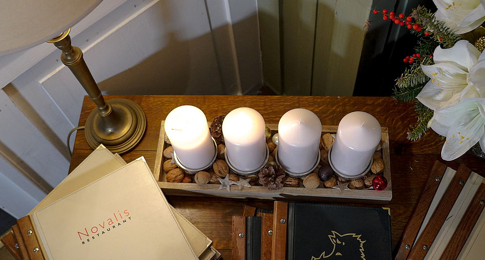 Vier weiße Kerzen auf Holztablett und goldene Lampe auf festlich gedecktem Tisch.